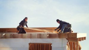 Workers constructing roof beam against sky during sunny day